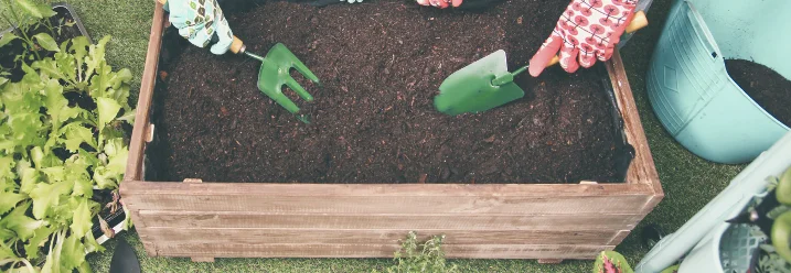 Drei Personen befüllen Hochbeet mit Erde